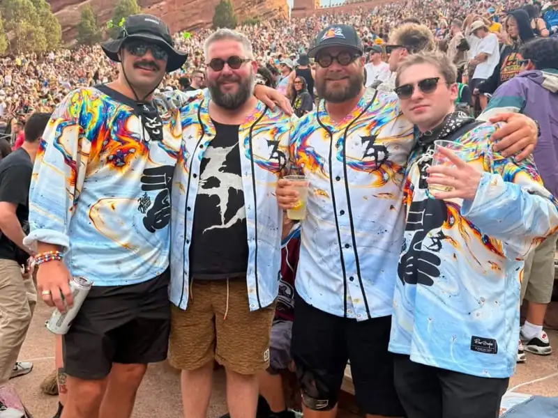 Four customers wearing matching light-blue, multicolor hockey and baseball jerseys at an outdoor concert.