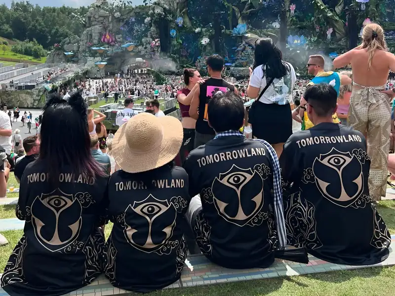 Four customers seen from behind in matching black-and-gold Tomorrowland jerseys, watching the festival stage.